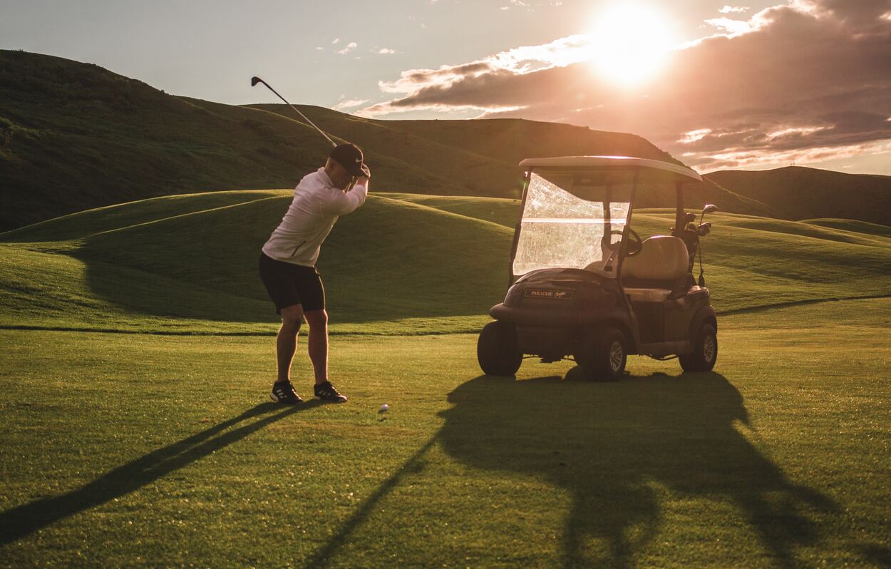 Golf cart and a golfer practicing his swing at sunset.